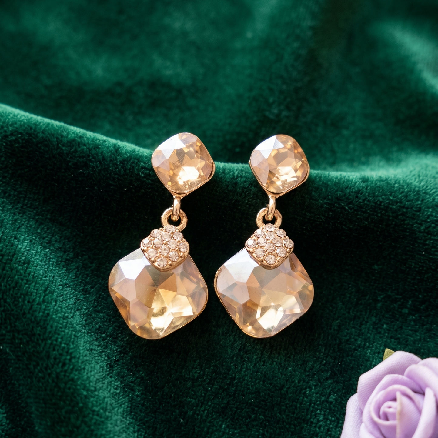 Gold earrings with faceted stones on a green fabric background