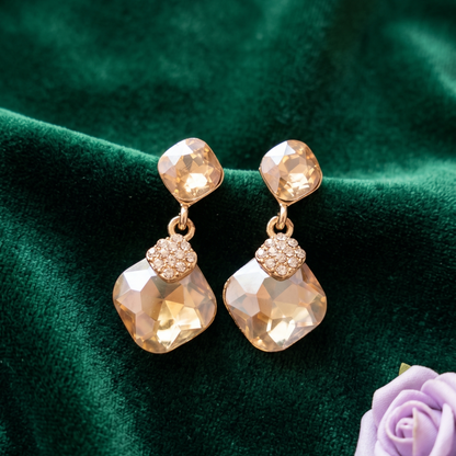 Gold earrings with faceted stones on a green fabric background