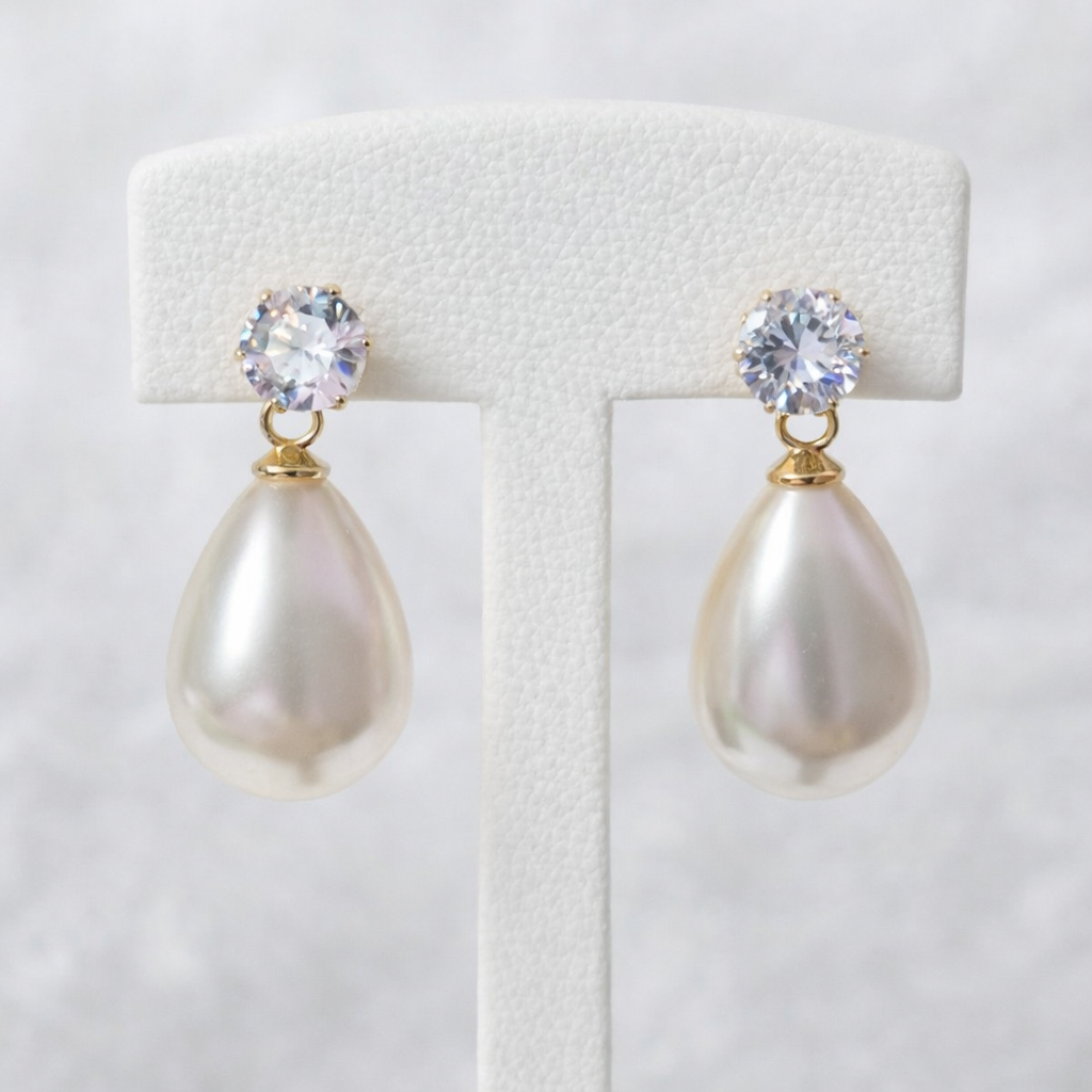 Pearl earrings with crystal tops on a white stand against a light gray background