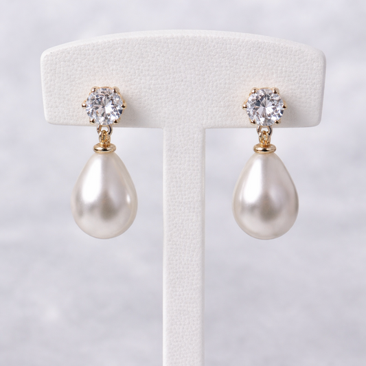 Pearl earrings with crystal tops on a white stand against a light gray background