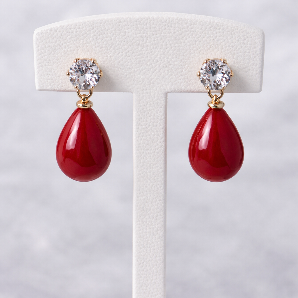 Red teardrop earrings with gold accents on a white earring stand against a light gray background