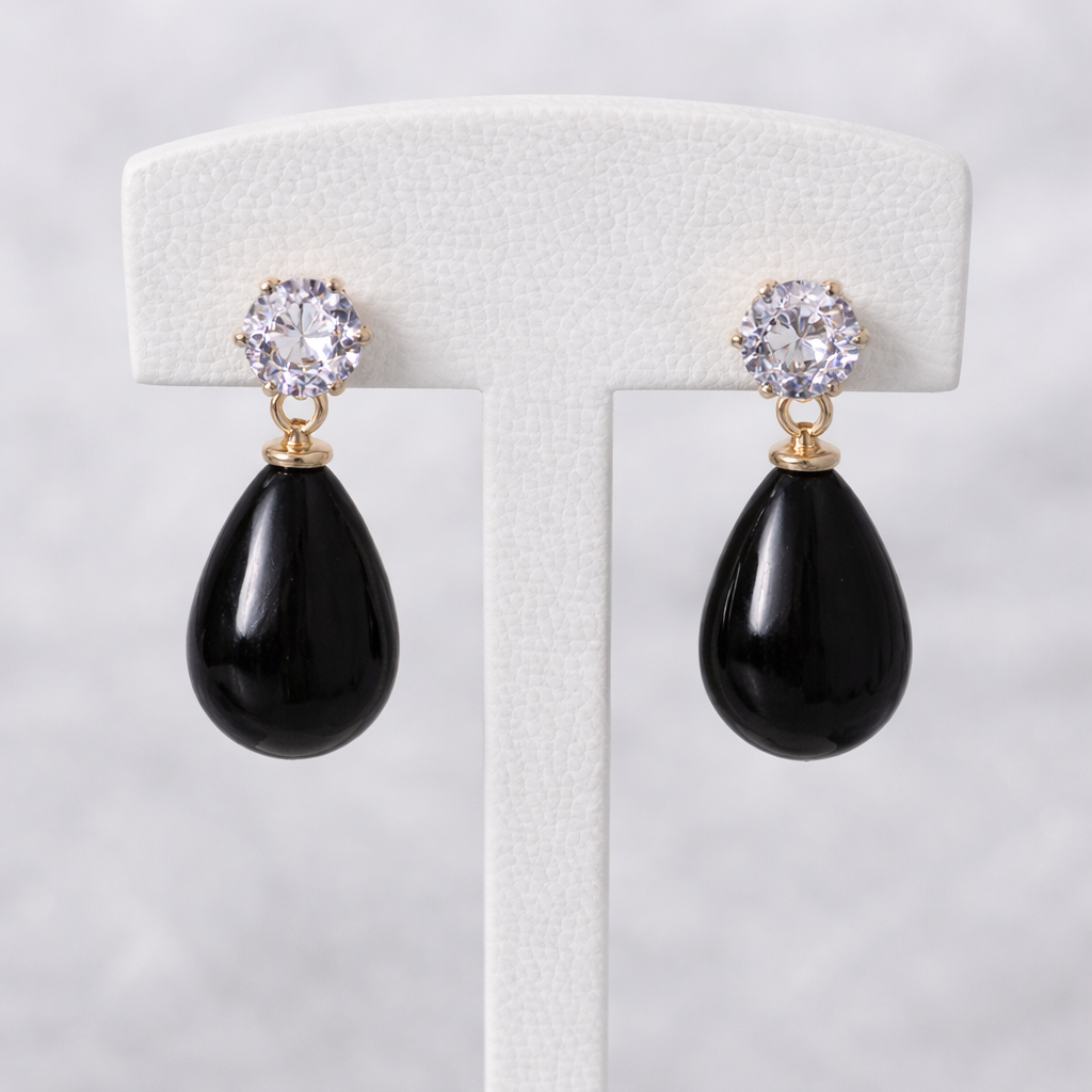 Black teardrop earrings with gold and crystal accents on a white stand.